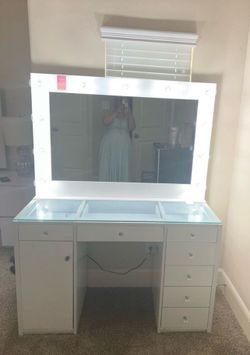 This Maklaine vanity desk features a white finish, seven drawers with crystal-like knobs, and a glass tabletop.