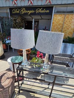 The pair of table lamps features clear glass bases with gray fabric shades.