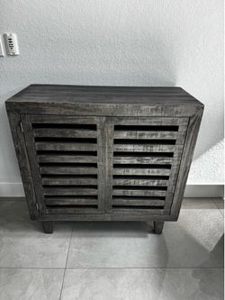 Rustic wooden storage cabinet has a weathered gray finish. This piece is constructed from solid wood with two louvered shutter-style doors. The interi
