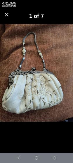 vintage-style ivory fabric evening bag features an ornate, antique-finish metal kiss-lock frame and a beaded top handle.