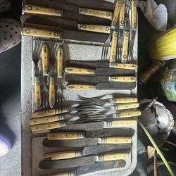 A collection features a mix of vintage silver-plated/sterling flatware, bone-handled cutlery, and handcrafted serving pieces.