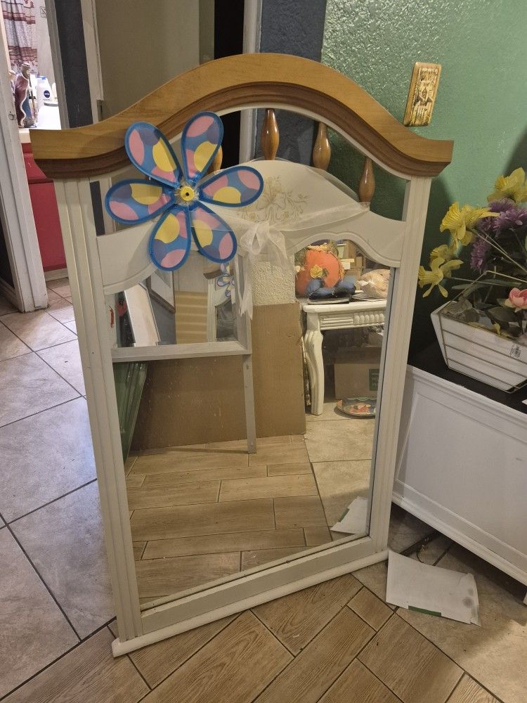 white wooden dresser mirror with a light wood top and an attached flower pinwheel decoration. 