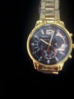 New gold stainless steel watch with a black chronograph-style dial. This timepiece has a link bracelet still wrapped in protective plastic and feature