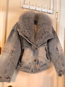 Chamarra de mezclilla azul para mujer, con cuello grande de peluche gris y forro acolchado color crema. Tiene bolsillos con cierre y bonitos detalles 