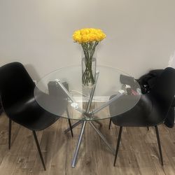 Modern round glass dining table with chrome base + 2 black chairs.