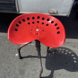 vintage farmhouse stool features a vibrant red tractor seat mounted on rustic industrial pipe legs.