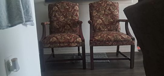 Sturdy pair of armchairs with dark wood frames and tapestry-style upholstery. The fabric has a multi-colored leaf and floral pattern in shades of burg