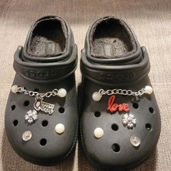 Black fur-lined Crocs clogs with Jibbitz shoe charms, pearl chains and decorative flower accents. Size 7