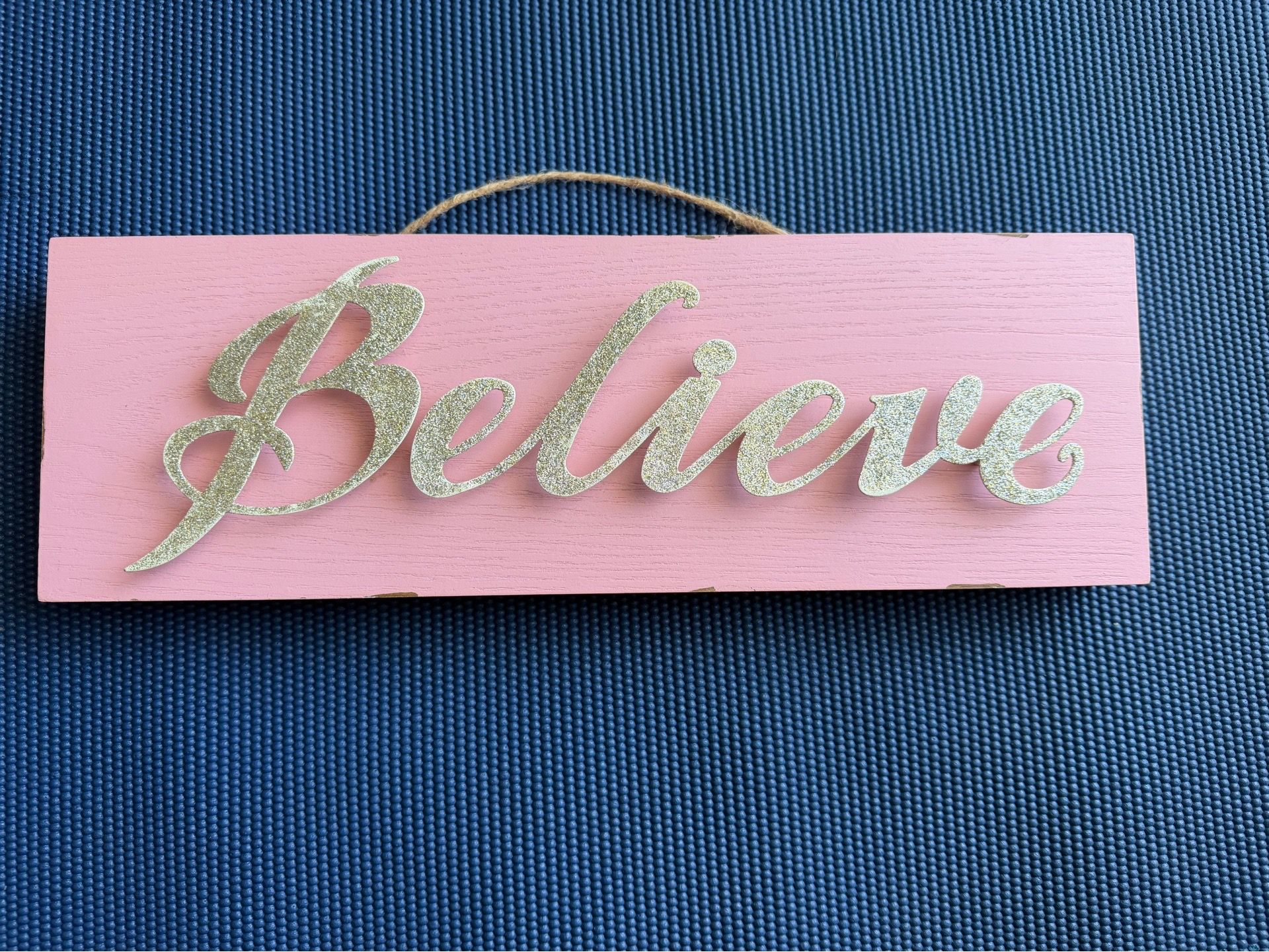 A pink wooden table decor sign featuring gold glitter "Believe" lettering, $30 or best offer