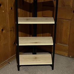 This four-tier shelving unit features an industrial, minimalist design that combines light-toned wooden shelves with a black metal frame. It is a vers