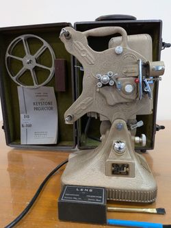 vintage Keystone 16mm movie projector, likely from the A-82 or similar 1930s–1950s cast-iron series, resting inside its original green-lined carrying