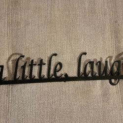 Black Elizabeth Keith metal wall sign with the phrase "Wine a little, laugh alot" and a wine glass shape. 29" L x 6" W