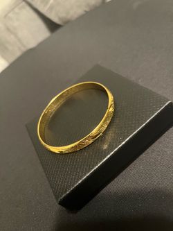 Shiny gold tone bangle bracelet. Has a cool etched pattern all around. Hinged design with a clasp closure. Looks really good with gold necklace