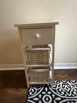 White wooden night stand with drawer and wicker baskets.