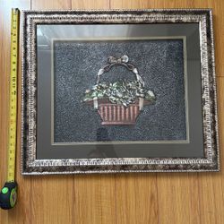 Decorative embossed metal relief artwork behind glass.
