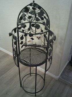 Decorative black wrought iron metal birdcage on stand with 2 white fake owls sitting on perch.