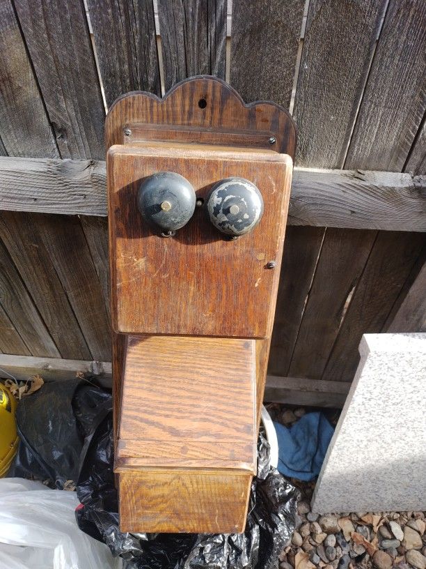 This is an antique wood hand crank wall telephone likely from the early 1900s. It is a collectible item. It features a wooden case dual bells and