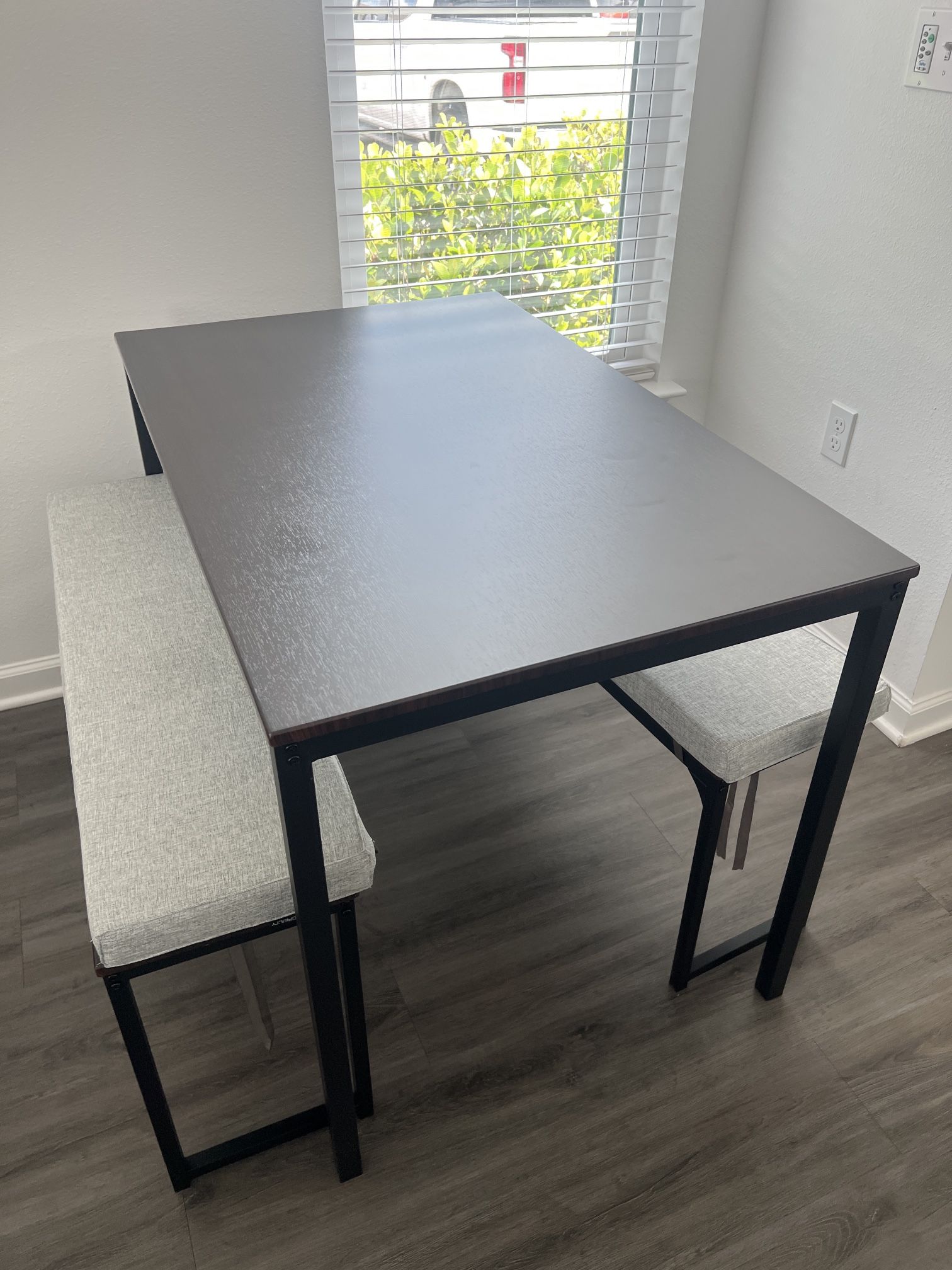 Brown table with black metal framing, with two benches + two cushions