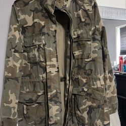Green and brown camo jacket with zipper and button closure, multiple pockets, and adjustable waist