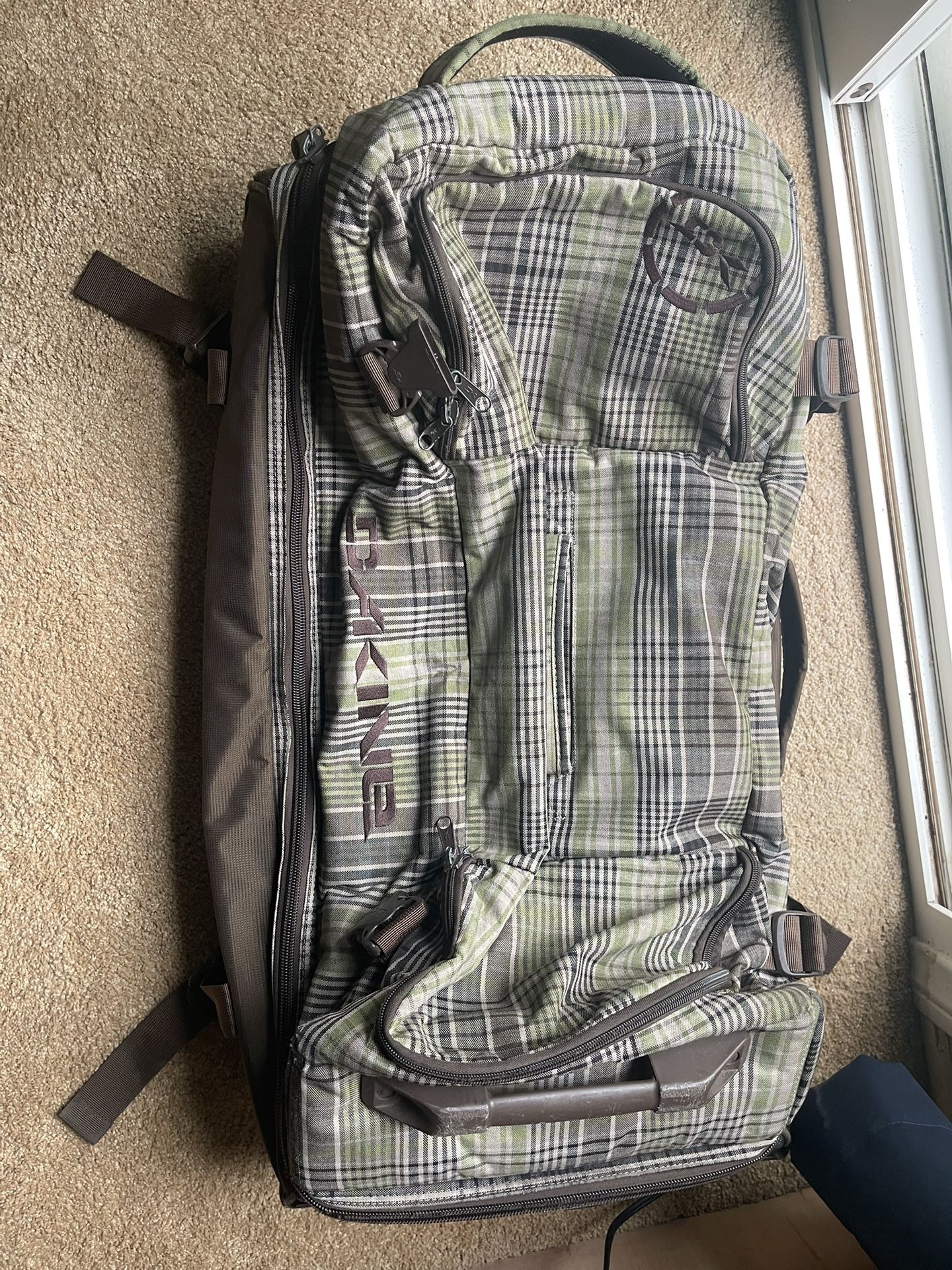 Large Dakine travel bag with plaid design and multiple compartments. Great for skiing snowboarding t