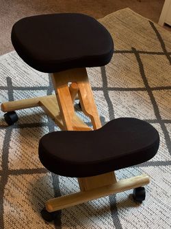 Ergonomic Wooden Kneeling Chair Wooden ergonomic kneeling chair has a light-colored natural wood frame with black fabric upholstered cushions. Exce