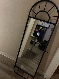 black arched full-length floor mirror with a decorative metal frame.
