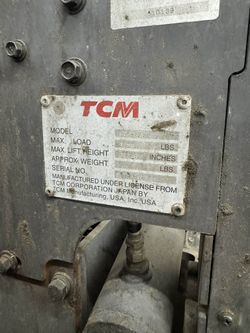Propane-powered TCM FCG25F9  forklift has a yellow and dark grey metal body. This industrial vehicle is equipped with a rear-mounted propane tank, a p