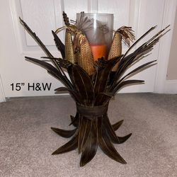 metal sheath of Corn husks surrounding a pillar candle in glass holder
