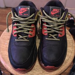 Nike Air Max 90 Black Asparagus (GS) is a children's sneaker featuring a black leather upper with red and asparagus-colored accents.