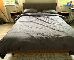 Gray upholstered queen bed with nightstands and mattress.