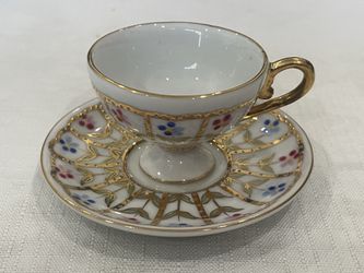 Miniature crown porcelain teapot and saucer with gold trim and floral decoration.