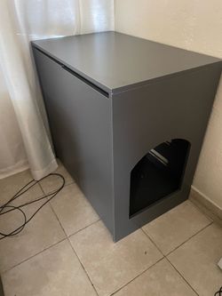 Este mueble es un gabinete moderno de color gris para ocultar cajas de arena de gatos, diseñado para integrarse