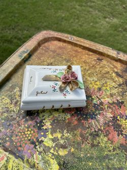 This is a vintage trinket box, possibly porcelain, with hand-painted floral decorations and a ribbon. It appears to