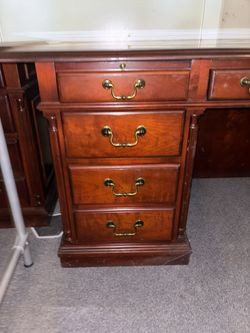 Traditional wooden executive desk with multiple drawers, featuring a dark cherry finish and brass-colored hardware.