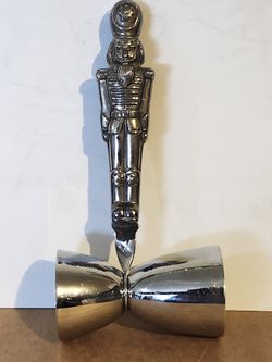 The image shows a Godinger silver-plated Christmas Nutcracker double jigger, used for measuring cocktail ingredients. 