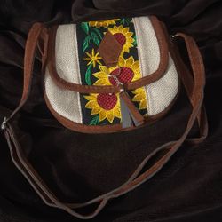 handmade crossbody bag features vibrant sunflower embroidery on a canvas and faux-suede body It is characteristic of artisanal handicrafts often found