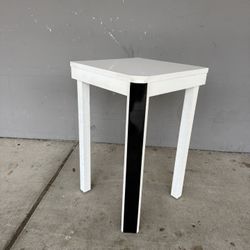 White square side table or coffee table. It has a simple design with four legs and can be used in the living room next to a sofa or armchairs, as a be