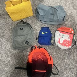 Six Different Bags: Under Armor Duffel, Jordan Backpack, Nike Lunchbox, Vans Backpack, Yellow Tote, And Kids Backpack. 