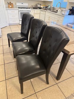 A set of 3 black leather button-tufted dining side chairs.