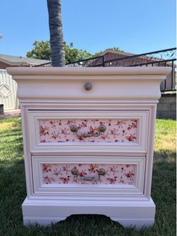pink vintage French Provincial nightstand features floral patterned drawer inserts and brass hardware.