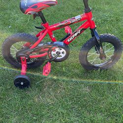 Huffy 12 Boys Rock It Red bike. Has scratches, decals peeling, minor rust, training wheels are worn, seat has tiny hole & pedals are scuffed on edges.