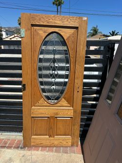 Solid oak entry door has a natural wood grain finish and a large oval leaded glass insert with a decorative diamond pattern. This door is pre-drilled