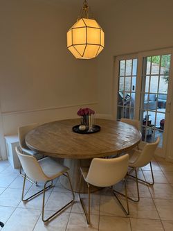 Round Wood Dining Table with Pedestal Base and 6 white pleather chairs with gold base.