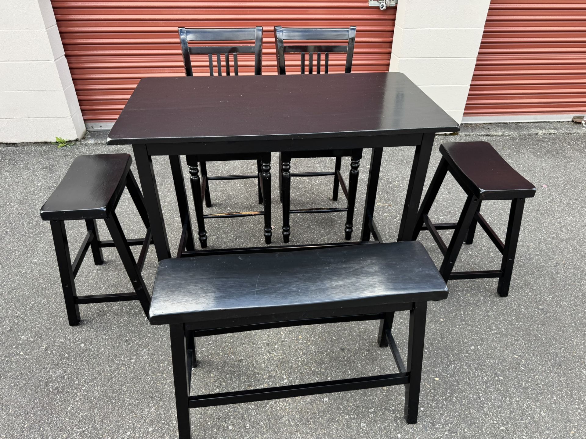 Black wooden table and two chairs and two stools and a bench