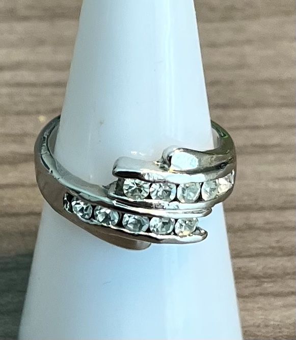 Elegant silver-tone ring with sparkling clear crystals. Features a wave-style design for modern appeal. Perfect as a statement or everyday accessory.