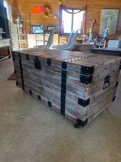 Rustic, reclaimed weathered-wood storage trunk and coffee table featuring black metal corner brackets, straps, and caster wheels