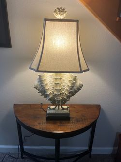 This vintage coastal ruffle clamshell table lamp features a striking sculpted clam shell base and an off-white tapered shade.