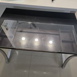 Wooden desk with a glass top and stainless steel legs. It measures 48 inches wide x 31 inches high and deep