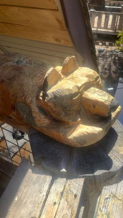 Hand carved wood bear sits on a 2 x 6