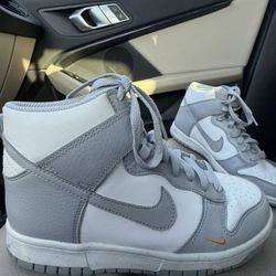 Nike Dunk High sneakers in a clean grey and white colorway with a small gold swoosh detail. Size 6Y (Youth) — fits like a Women’s 7